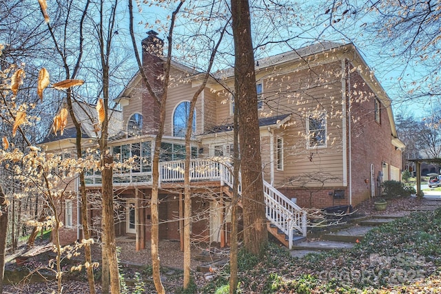 rear view of house featuring brick siding, stairway, a chimney, and a wooden deck