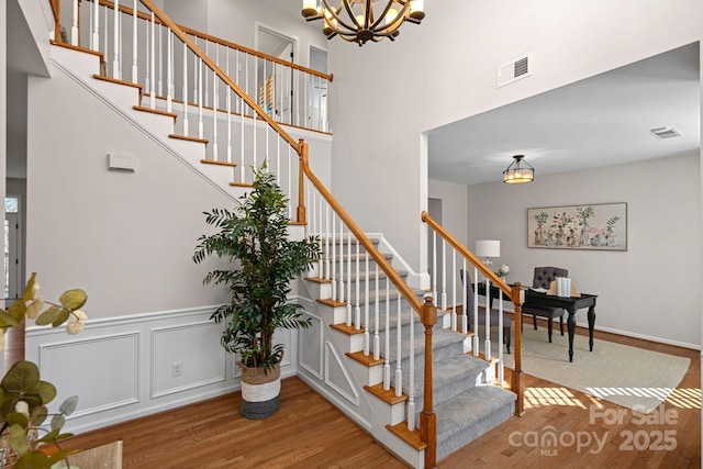 staircase with a high ceiling, visible vents, an inviting chandelier, and wood finished floors