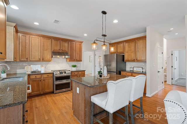 kitchen featuring visible vents, appliances with stainless steel finishes, a center island, under cabinet range hood, and a sink