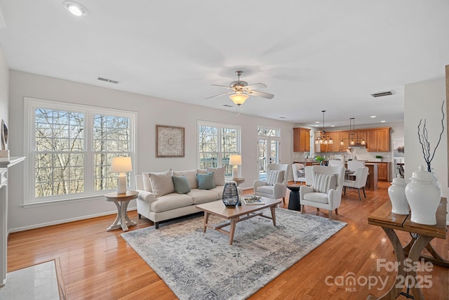 living area featuring light wood-style floors, visible vents, baseboards, and a ceiling fan