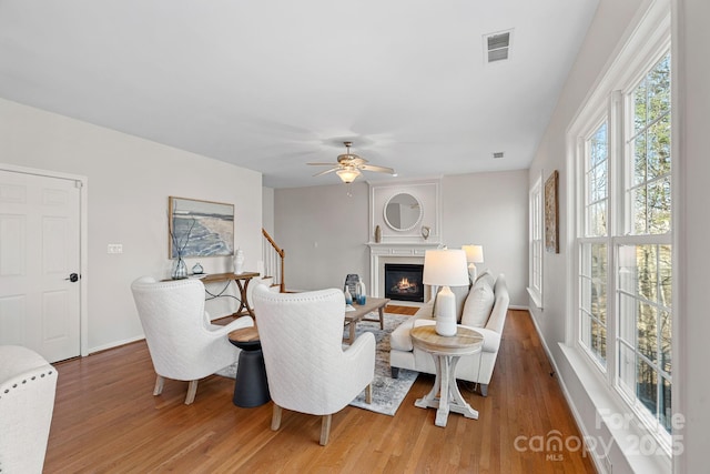 living area featuring wood finished floors, visible vents, a ceiling fan, stairs, and a glass covered fireplace