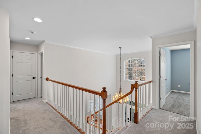 hallway featuring a notable chandelier, an upstairs landing, baseboards, carpet, and crown molding