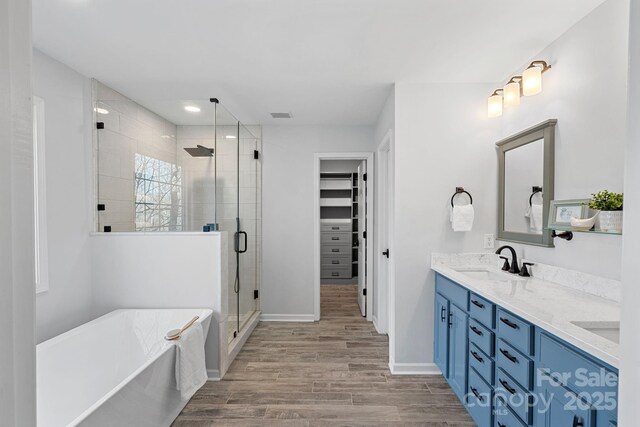 full bathroom with visible vents, wood finished floors, a walk in closet, a shower stall, and a sink