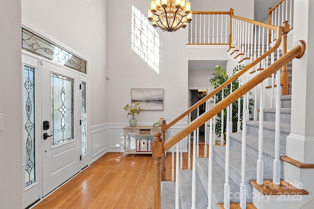 foyer featuring a decorative wall, a wainscoted wall, wood finished floors, a towering ceiling, and an inviting chandelier