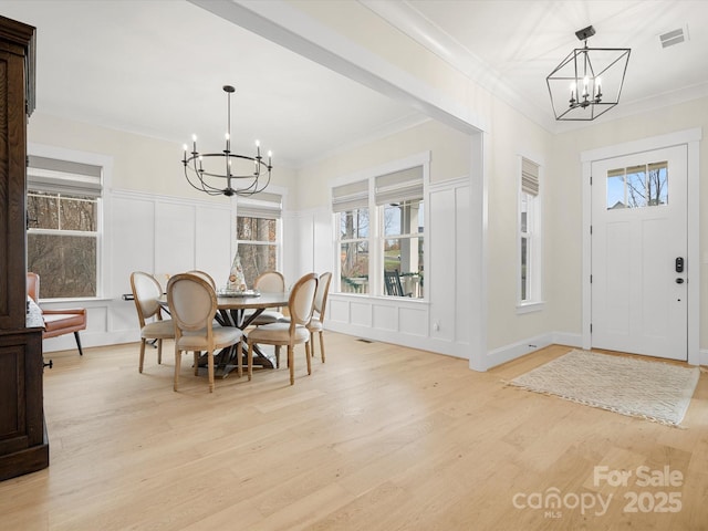 dining space featuring an inviting chandelier, visible vents, a decorative wall, and ornamental molding