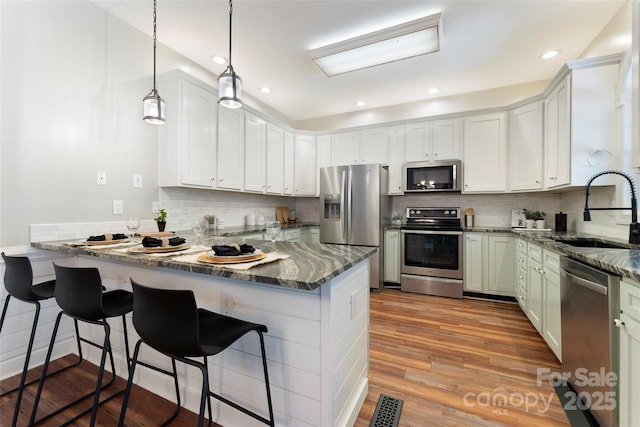 kitchen with stainless steel appliances, white cabinets, a sink, and a peninsula