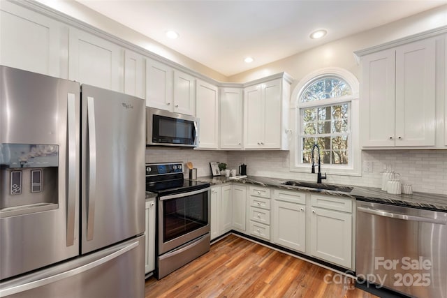 kitchen with a sink, white cabinets, appliances with stainless steel finishes, decorative backsplash, and dark stone countertops