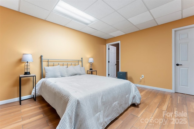 bedroom featuring a paneled ceiling, light wood finished floors, and baseboards