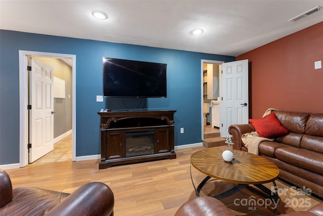 living area with a glass covered fireplace, baseboards, visible vents, and light wood finished floors