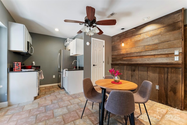 dining area featuring stone finish flooring, a ceiling fan, visible vents, and baseboards