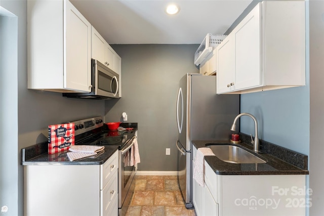 kitchen featuring white cabinets, stone finish floor, appliances with stainless steel finishes, dark stone countertops, and a sink