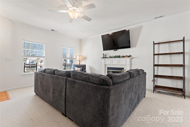 living room featuring visible vents, a ceiling fan, a textured ceiling, a glass covered fireplace, and crown molding