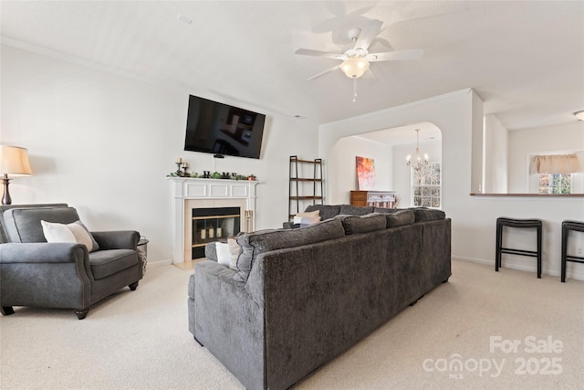 living room featuring a glass covered fireplace, light colored carpet, ceiling fan with notable chandelier, and baseboards