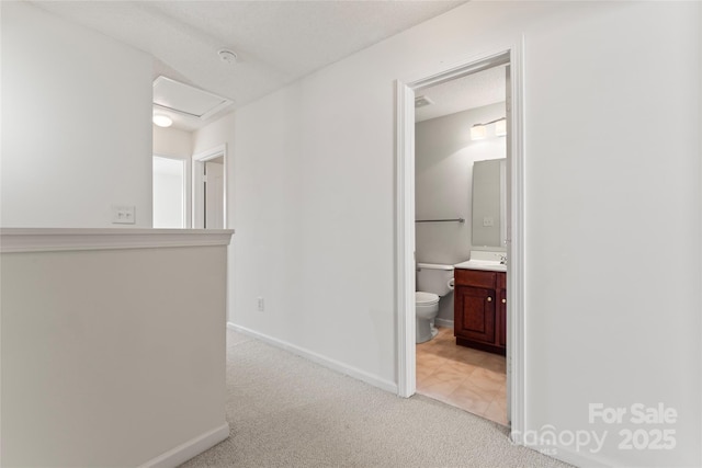 hallway with light colored carpet, attic access, baseboards, and a sink