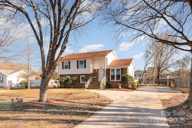 view of front of home with fence, concrete driveway, and brick siding