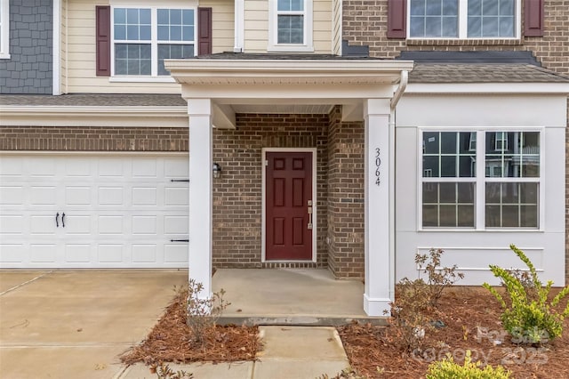 entrance to property featuring an attached garage, driveway, and brick siding