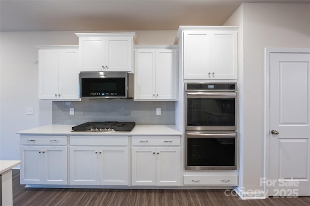 kitchen with dark wood-style flooring, stainless steel appliances, light countertops, backsplash, and white cabinetry