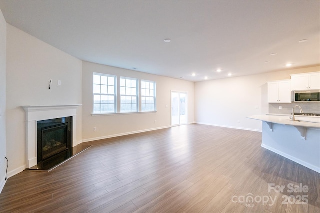 unfurnished living room with dark wood-style floors, recessed lighting, a fireplace with raised hearth, and baseboards