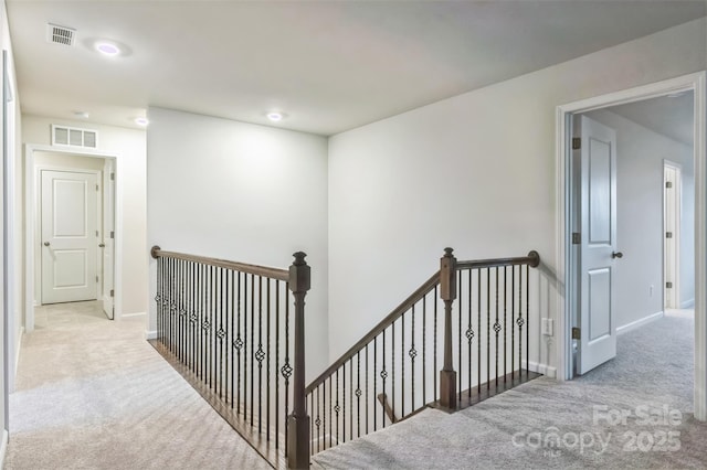 hallway with light carpet, visible vents, an upstairs landing, and baseboards