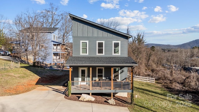 view of front of home featuring covered porch, fence, roof with shingles, a front lawn, and board and batten siding