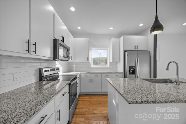 kitchen with stainless steel appliances, a sink, white cabinets, hanging light fixtures, and light wood-type flooring