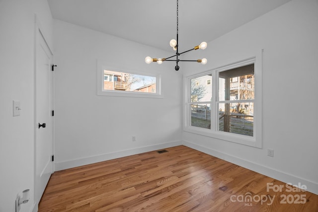 unfurnished dining area with baseboards, visible vents, light wood finished floors, and an inviting chandelier