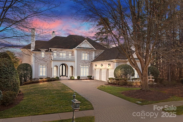 view of front facade featuring a garage, a balcony, decorative driveway, a yard, and stucco siding