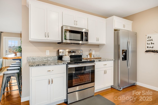 kitchen featuring stainless steel appliances, baseboards, white cabinets, light stone countertops, and light wood finished floors