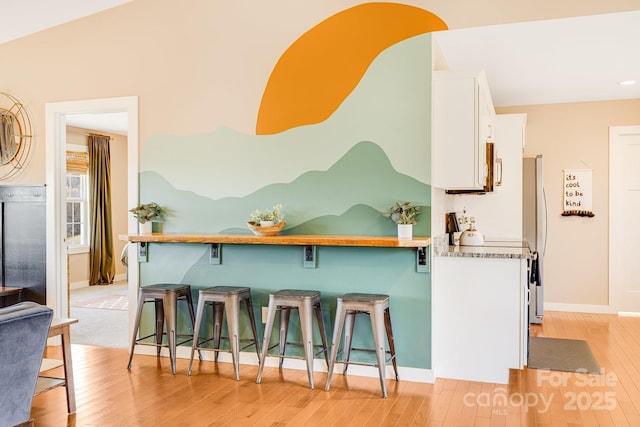 kitchen featuring light wood finished floors, freestanding refrigerator, white cabinetry, a kitchen breakfast bar, and baseboards