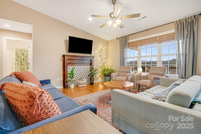 living area featuring baseboards, visible vents, ceiling fan, wood finished floors, and vaulted ceiling