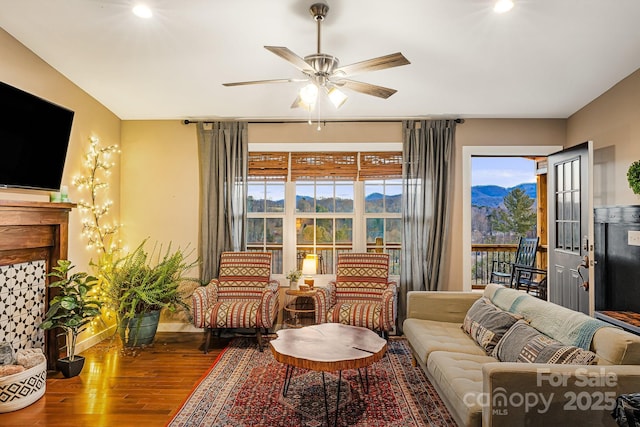 living area featuring baseboards, a fireplace, a ceiling fan, and wood finished floors