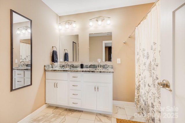 full bathroom featuring double vanity, marble finish floor, baseboards, and a sink