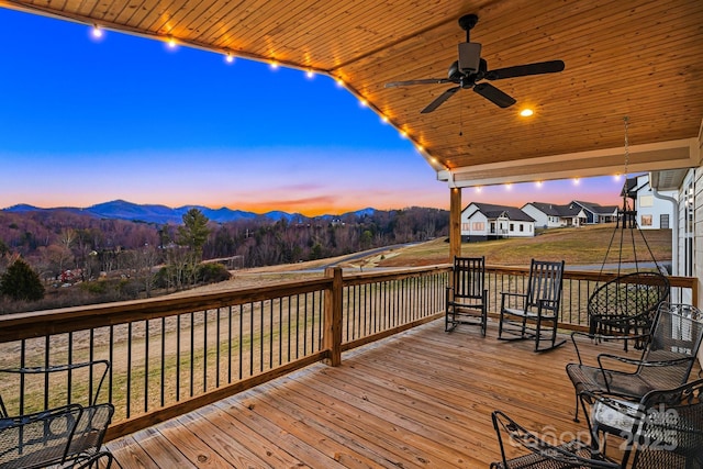 deck at dusk with a yard, ceiling fan, and a mountain view