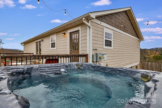 rear view of property with a deck, fence, and a hot tub