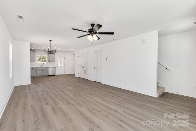 unfurnished living room with visible vents, stairway, light wood-style floors, a sink, and baseboards