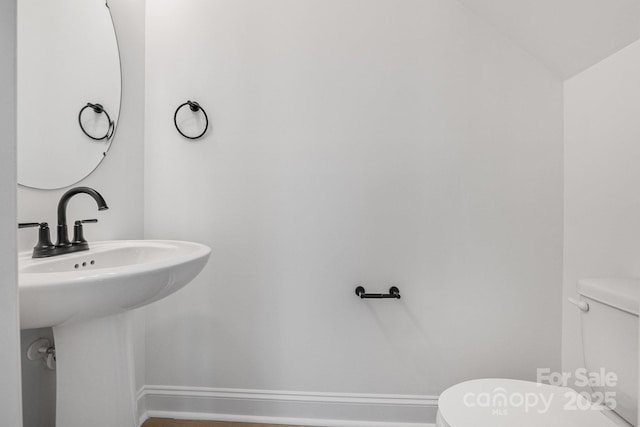 half bath with toilet, baseboards, a sink, and lofted ceiling