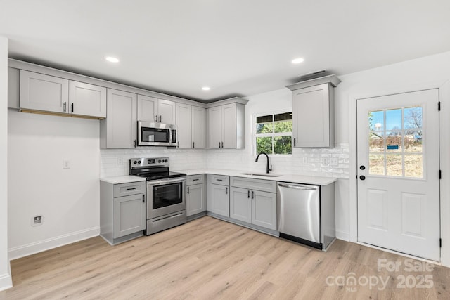 kitchen with stainless steel appliances, tasteful backsplash, light countertops, light wood-style floors, and a sink