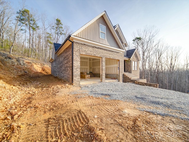 view of side of home with gravel driveway, an attached garage, board and batten siding, and brick siding