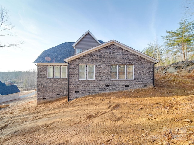 view of property exterior featuring crawl space, brick siding, and roof with shingles