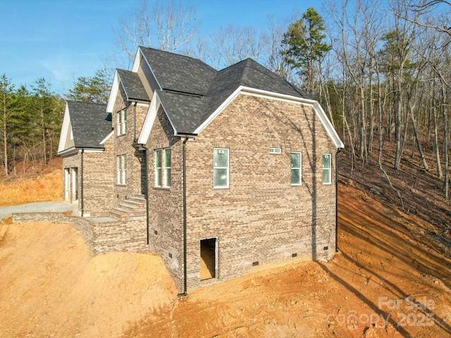 view of home's exterior with crawl space, a shingled roof, and brick siding