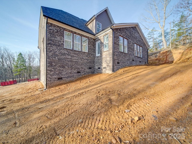 view of side of property with brick siding, crawl space, and a shingled roof