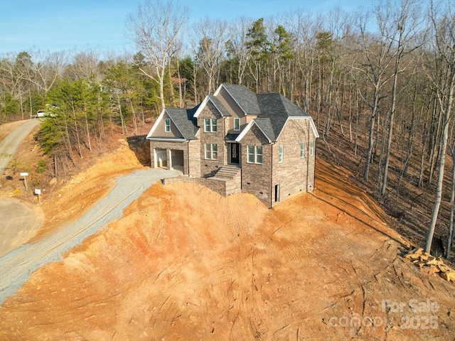 view of front of house with driveway, a garage, roof with shingles, crawl space, and a wooded view