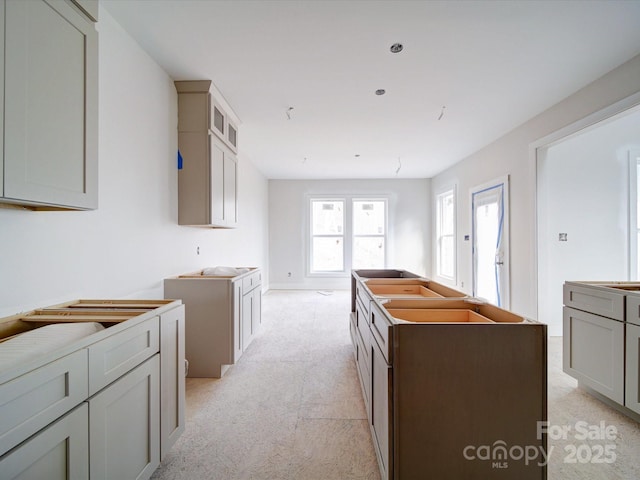 kitchen with light carpet, a kitchen island, glass insert cabinets, and gray cabinets