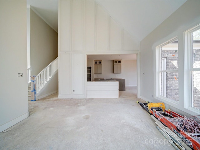 unfurnished living room with vaulted ceiling, stairway, and baseboards