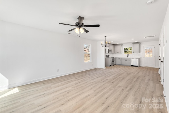 unfurnished living room featuring a healthy amount of sunlight, a sink, light wood-style flooring, and baseboards