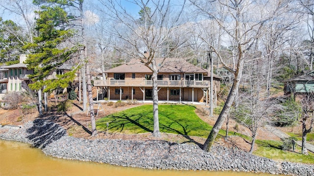 rear view of property with a yard, a deck with water view, and brick siding