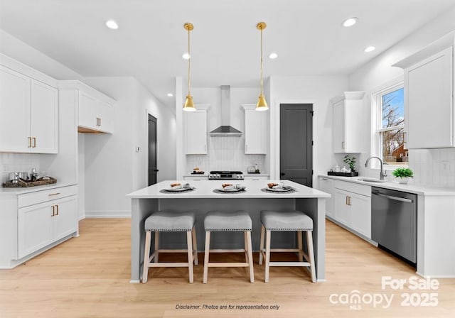 kitchen featuring wall chimney range hood, a kitchen island, light countertops, and stainless steel dishwasher