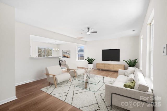 living room featuring ceiling fan with notable chandelier, wood finished floors, visible vents, and baseboards