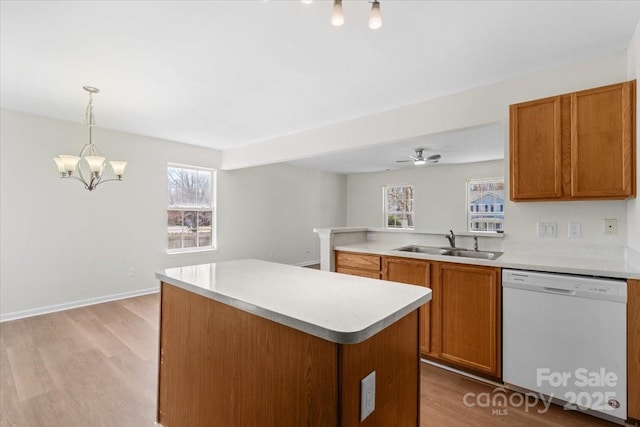 kitchen with brown cabinetry, dishwasher, hanging light fixtures, light countertops, and a sink