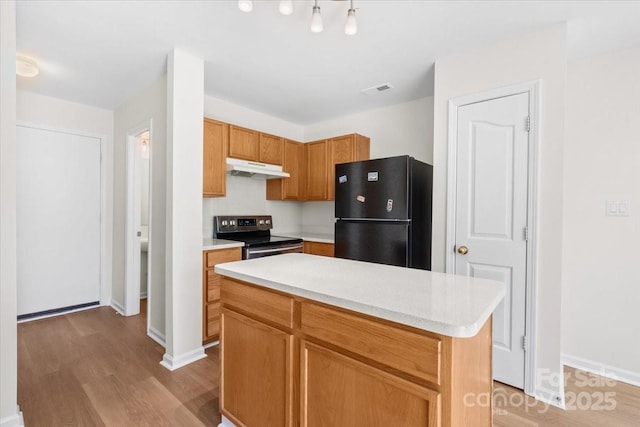 kitchen with under cabinet range hood, electric stove, light countertops, freestanding refrigerator, and a center island